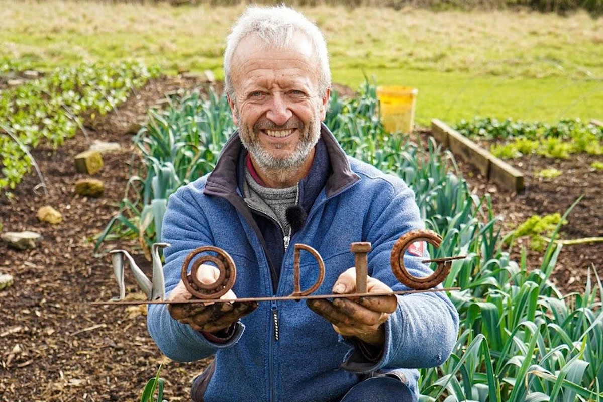 A smiling gardener holding a handful of worm casts in a vegetable garden